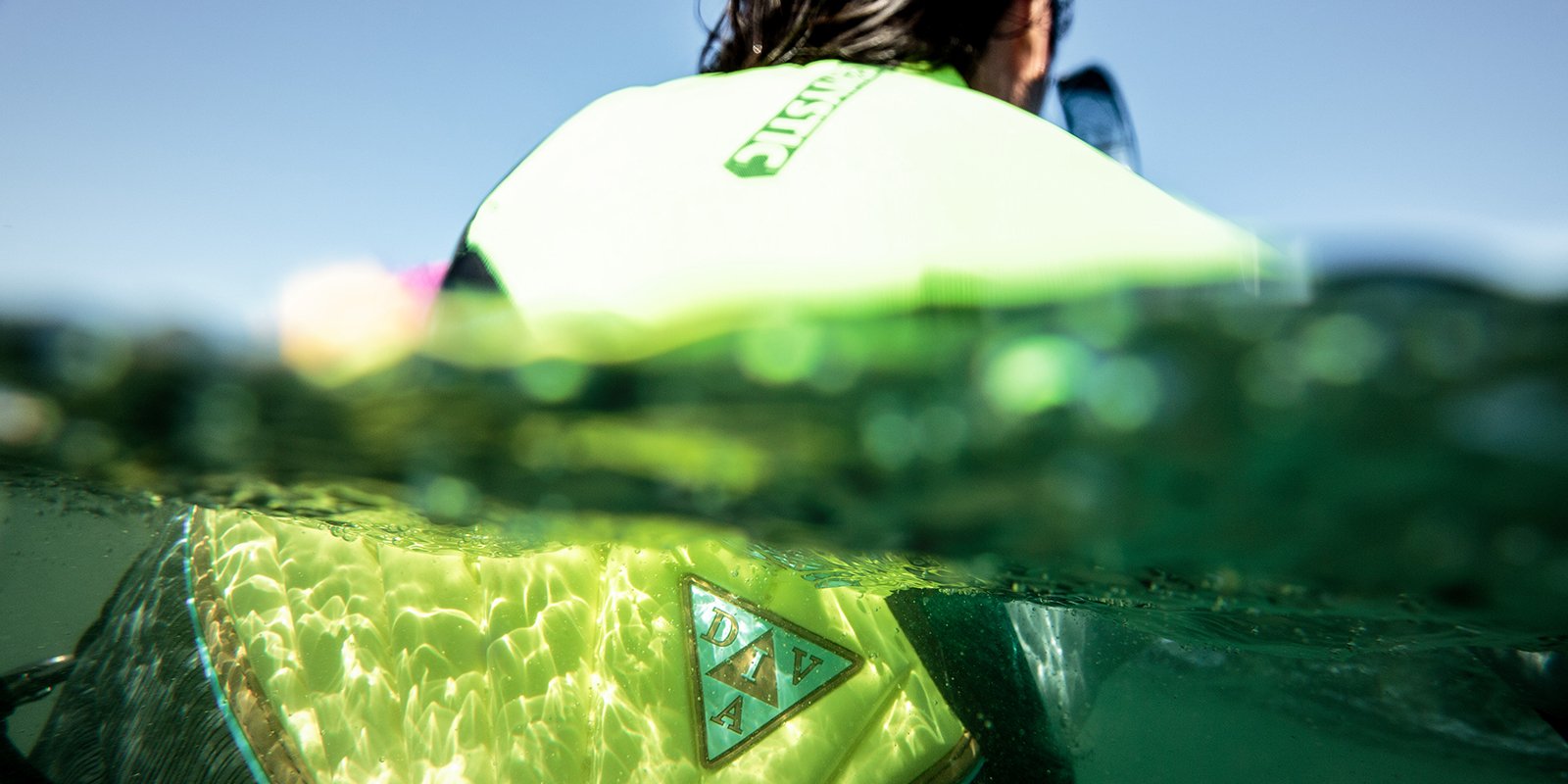 Pessoa praticando kitesurf com colete verde na água, close em equipamento da Orca Sports